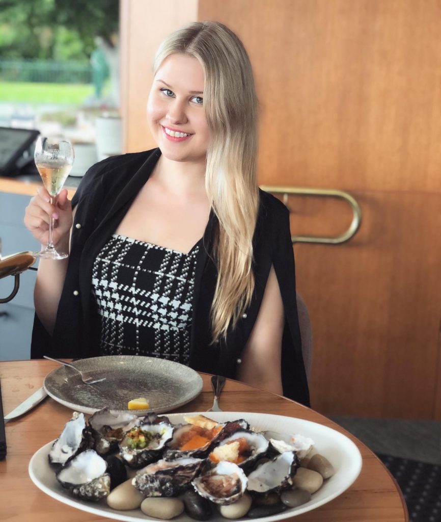 Jordan Cannon, founder of Everyday Nourished, smiling while enjoying a plate of oysters